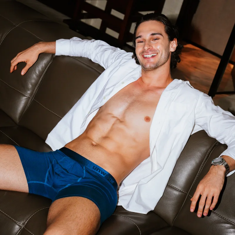 smiling man wearing Unwear modal boxer briefs sitting on a leather sofa with arms spread wide