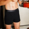 model wearing unwear onyx black modal boxer shorts standing beside a wooden table